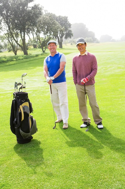 Golfing friends smiling at camera holding clubs