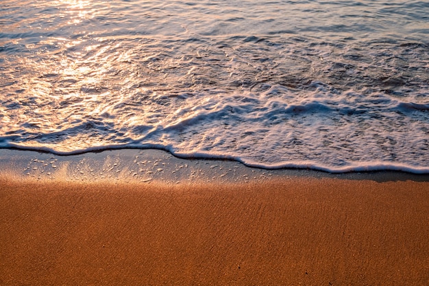 Golfschuim en blauwe oceaan op het strand bij zonsopgang.