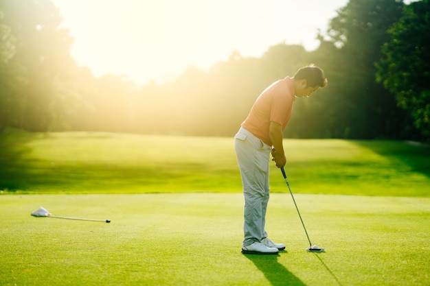 Golfspeler die golfbal zet aan gat in golfcursus op zonsondergang voor de zomervakantie.