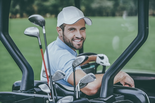 Golfspeler in golfkar. achteraanzicht van jonge gelukkige mannelijke golfspeler die een golfkar bestuurt en over schouder kijkt