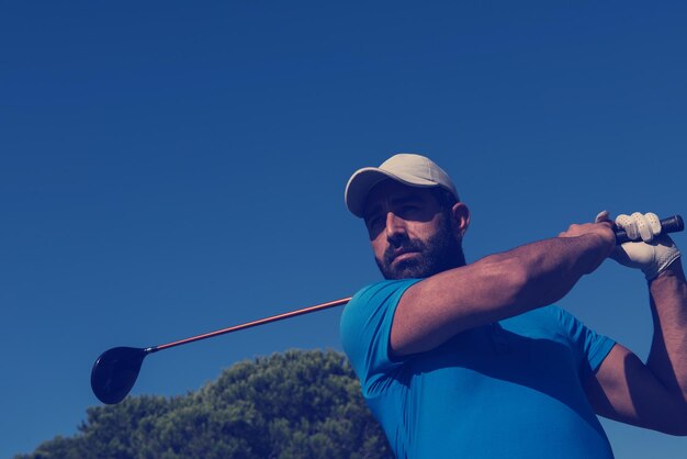 Foto golfspeler raakt schot met club op koers op mooie ochtend met zonnevlam op de achtergrond