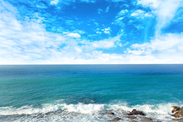 Golven die de kust breken bij blauwe zee en lucht met witte wolken