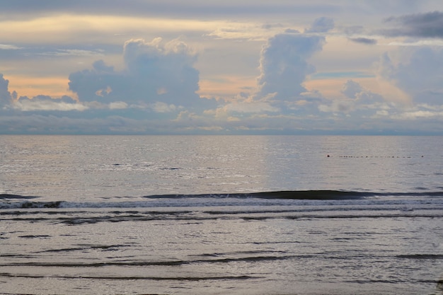 Golven slaan op het strand met oranje lucht en witte wolken in de ochtend.