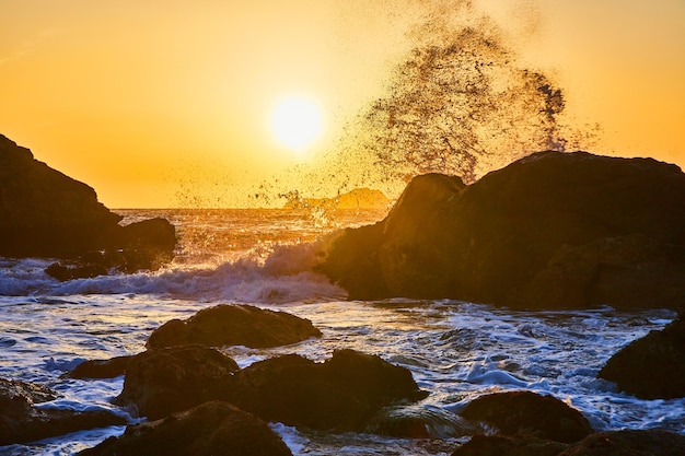 Golven slaan tegen rotsblokken met levendige zonsondergang aan de westkust