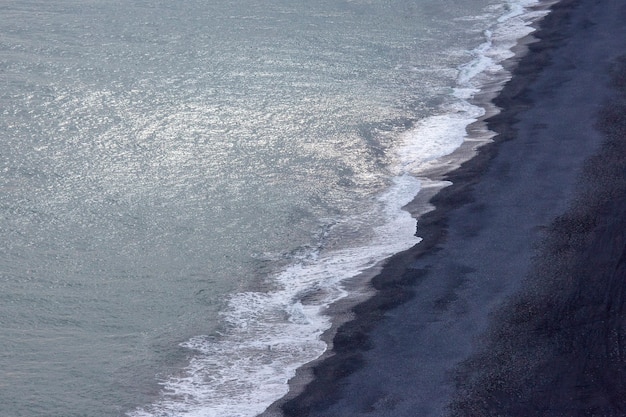 Golven van de Atlantische oceaan vallen vanaf een hoogte op het zwarte zand van het strand van IJsland