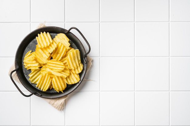 Golvende licht gezouten aardappelchips op witte keramische vierkante tegel tafel achtergrond bovenaanzicht plat lag met kopieerruimte voor tekst