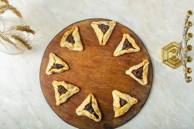メノラーと小麦の穂の横にある木の板にプリムのユダヤ教の祝日のために伝統的なゴメンタシクッキー