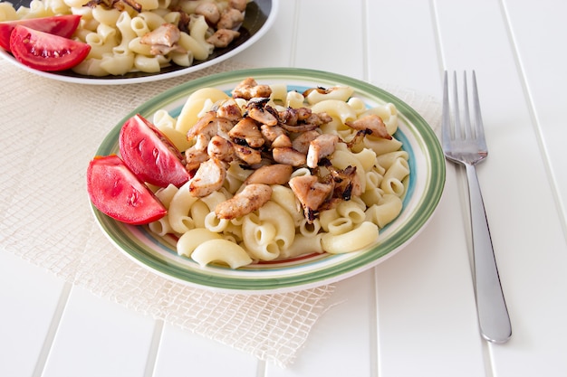 Gomiti Pasta with fried chicken and onion pieces with tomato and fork.