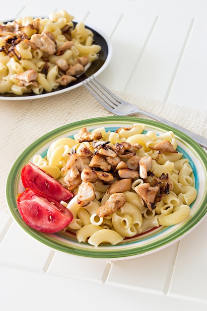 Foto gomiti pasta con pollo fritto e pezzi di cipolla con pomodoro e forchetta.