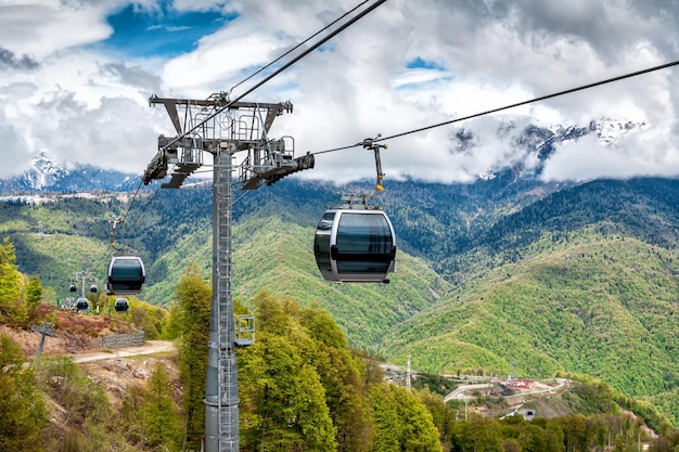 Photo gondola lift against the backdrop of a green forest and snowcapped mountains