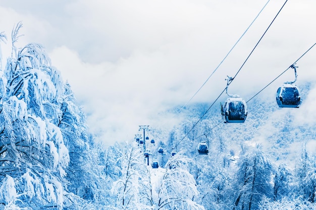 Gondola lift in ski resort in winter mountains during snowfall. Rosa Khutor, Sochi, Russia. Beautiful snow-covered forest, winter landscape