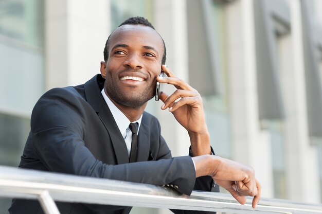 Good business talk. Happy young African man in formalwear talking on the mobile phone and smiling while standing outdoors