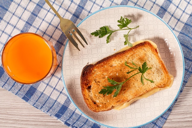 Good and delicious food and beverages for breakfast. Toast with butter and cheese on plate with fork and glass of orange juice on kitchen napkin. Top view.