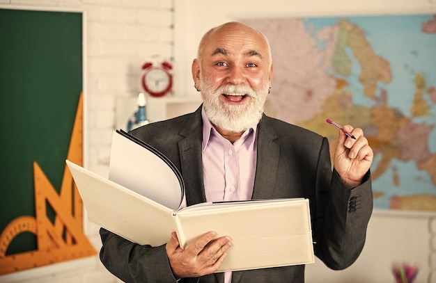 Good idea to study back to school math education in school\
bearded man give marks write notes in book happy senior lecturer\
make notes teacher of geography classroom with map and\
blackboard