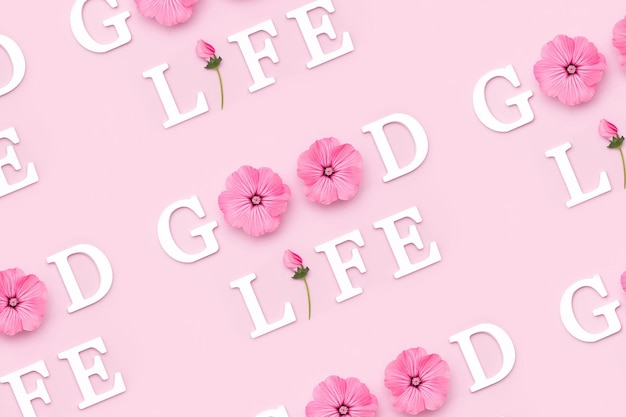 Good life Creative inspirational pattern made with motivational quotes from white letters and beauty natural flowers on pink background