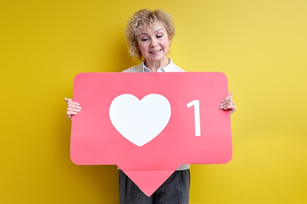 good-looking aged woman enjoy being active in internet blogging, holding heart like sign in hands