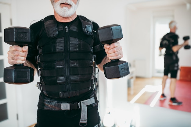 Фото Красивый и позитивный старший мужчина делает упражнения в костюме для электрической мышечной стимуляции.