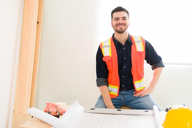 Good-looking architect smiling and making eye contact while working on the construction plans for a new project