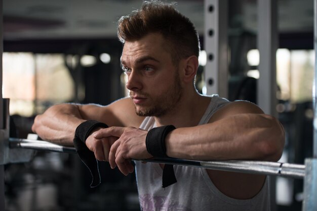 good looking and attractive young man with muscular body sitting on bench and relaxing in gym