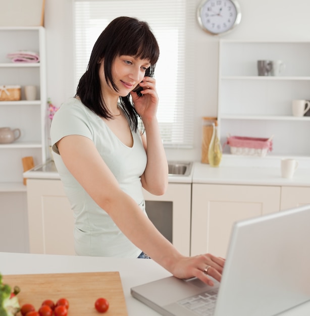 Good looking brunette female on the phone while relaxing with her laptop