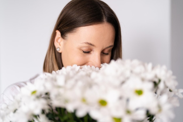 사진 잘 생긴 백인 여성은 신선한 흰 국화 꽃다발을 받아 행복한 꽃 냄새를 맡는다