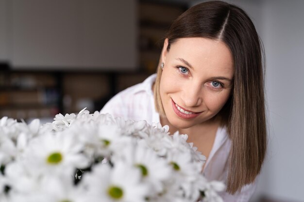 Good looking Caucasian woman smells flowers she is happy for get a fresh bouquet of white chrysanthemum