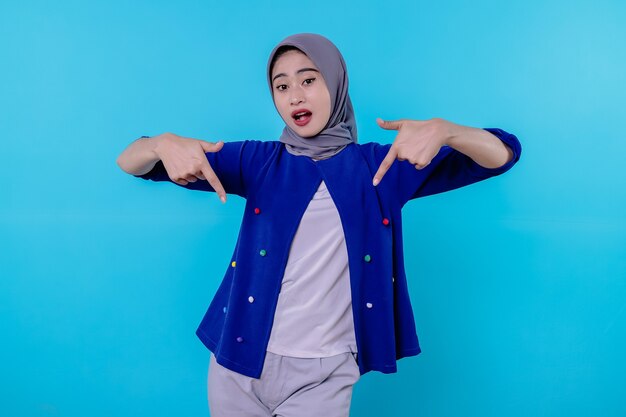 Good looking charismatic young woman with wearing hijab pointing down isolated on light blue background