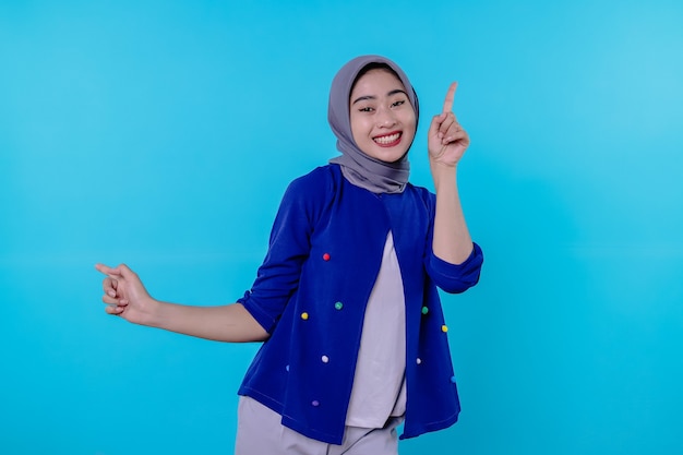 Good looking charismatic young woman with wearing hijab pointing isolated on light blue background