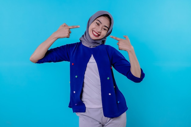 Good looking charismatic young woman with wearing hijab pointing isolated on light blue background