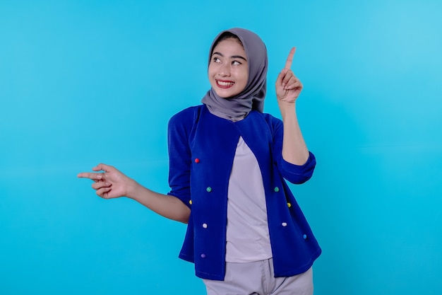 Good looking charismatic young woman with wearing hijab pointing isolated on light blue background