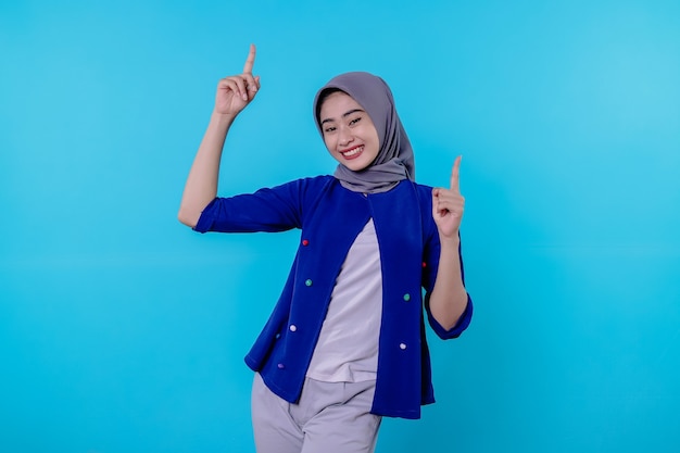 Good looking charismatic young woman with wearing hijab pointing up isolated on light blue background