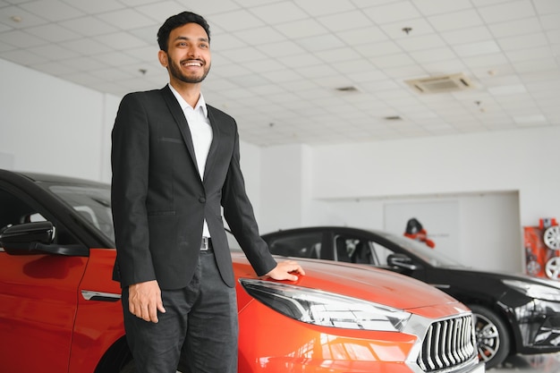 Good looking cheerful and friendly indian salesman poses in a car salon or showroom