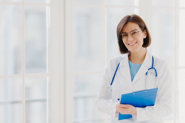 Good looking female expert creats medical prescription, writes down information in clipboard