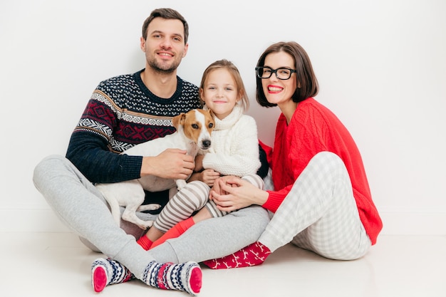 Good looking female and male sit together with their daughter and jack russell terrier dog