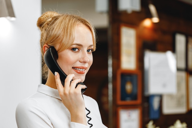 Addetto alla reception di hotel di bella donna amichevole parlando al telefono