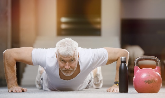 Good looking gray haired senior man in white shirt with water bottle. Sport and health care concept