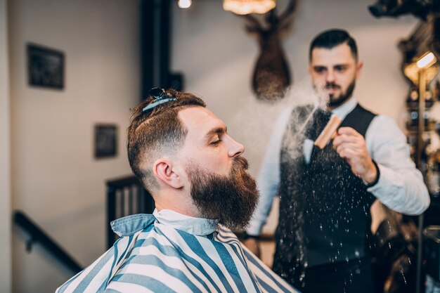 Good looking hipster young bearded man visiting hairstylist in barber shop.