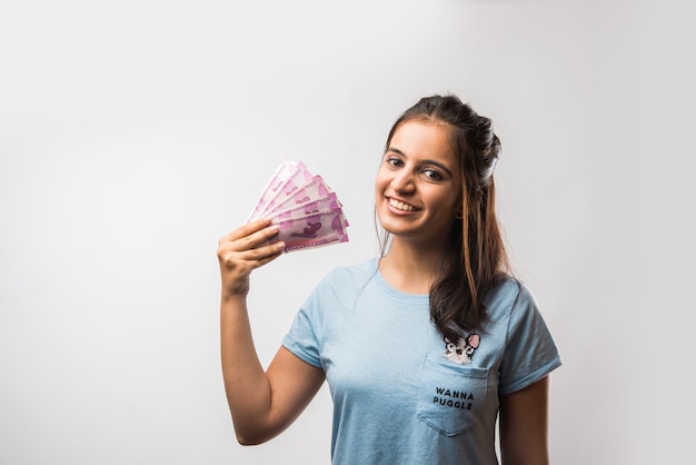 Good looking Indian Asian girl holding money fan consisting of new 2000 rupee notes, isolated over white background