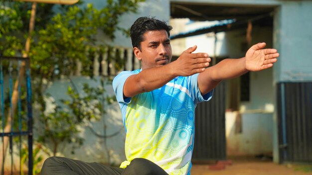 Photo good looking man in blue sport shirt and black pants sitting on yoga mat doing maditation with hand