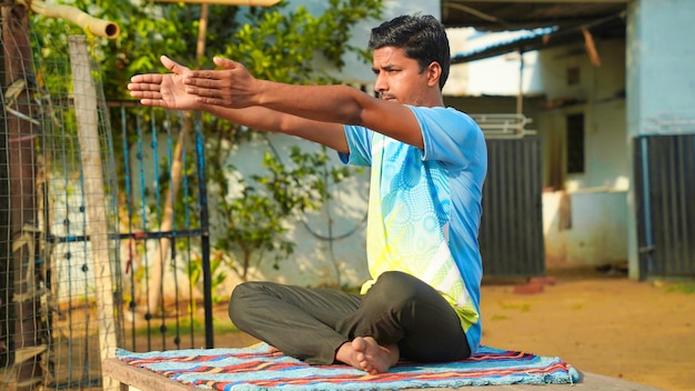 Good looking man in blue sport shirt and black pants sitting on yoga mat doing maditation with hand