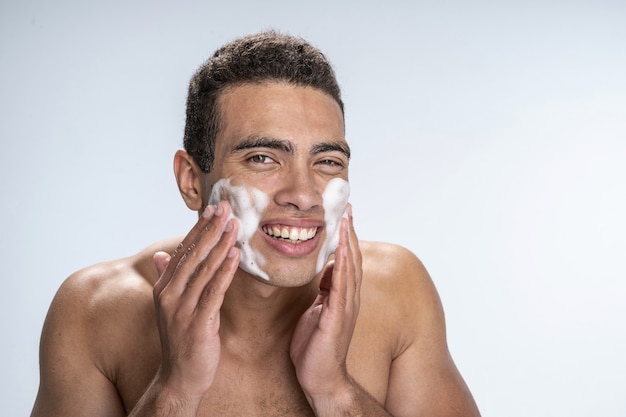 Good-looking man using special foam while washing his face