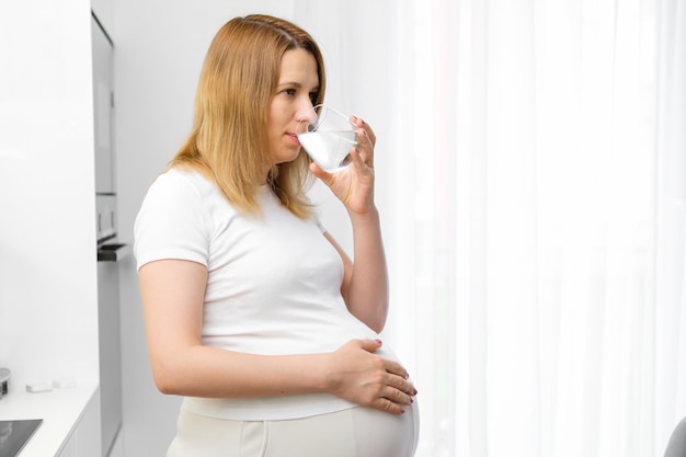 素敵な妊婦が台所に立って水を飲んでいる