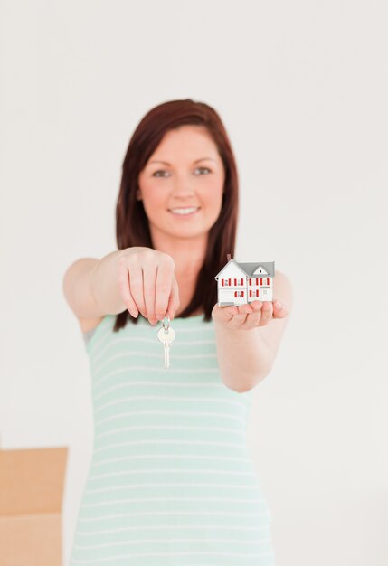 Photo good looking red-haired female holding a key and a miniature house standing on the floor