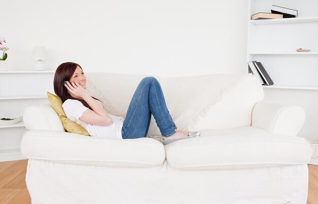 Good looking red-haired woman having a conversation on the phone while lying on a sofa