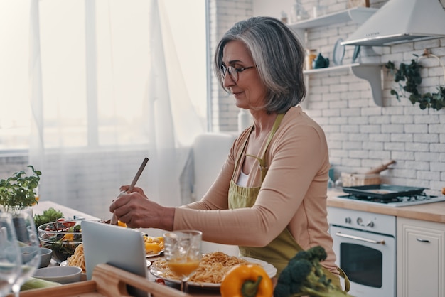 Good looking senior woman in apron cooking healthy dinner while spending time at home