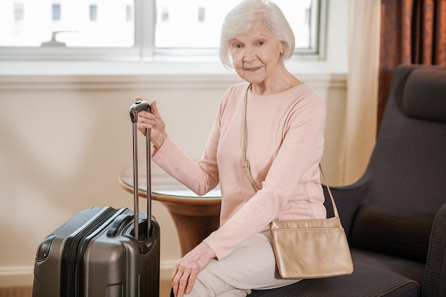 Good-looking senior woman sitting with a suitcase in a hotel room