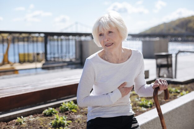 Good-looking unhappy ill woman suffering from heart attack while sitting on the bench and waiting for husband