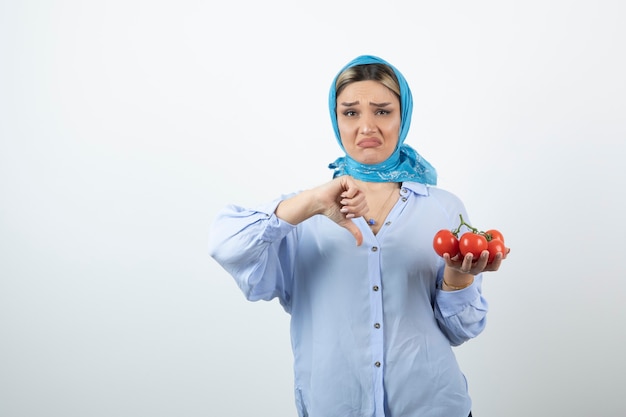 Фото Красивая женщина в шали показывает большой палец вниз и держит красные помидоры