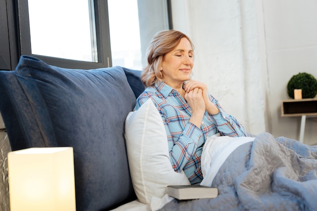 Good-looking woman. Pleasant calm mature lady holding connected hands in front of her and meditating during morning routine