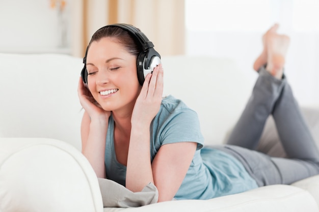 Good looking woman with headphones posing while lying on a sofa